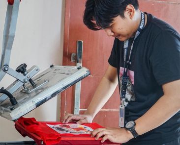 Proses press pada sablon manual dan DTF menggunakan mesin heat press untuk hasil cetakan yang tahan lama dan berkualitas tinggi.